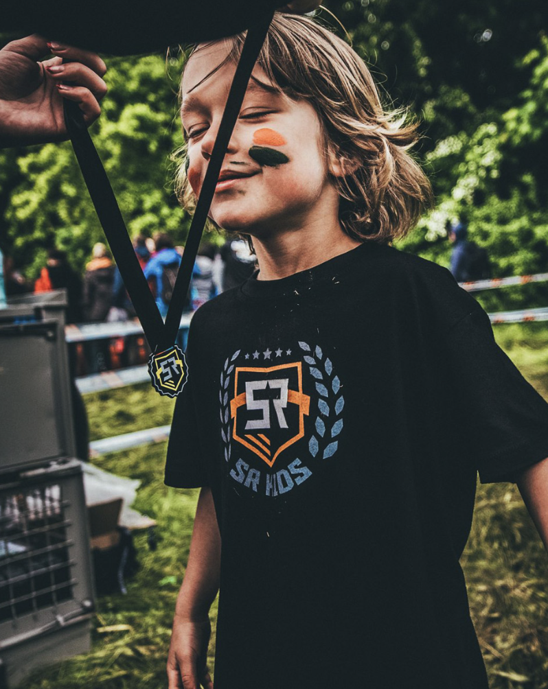 Dziecko z zamkniętymi oczami i wymalowaną twarzą dumnie prezentuje medal Survival Race Kids po ukończeniu trasy.